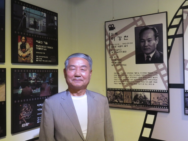 기벌포영화관 벽면에 전시된 이강천 감독 앞에서 아들 이재준씨가 기념촬영하고 있다.